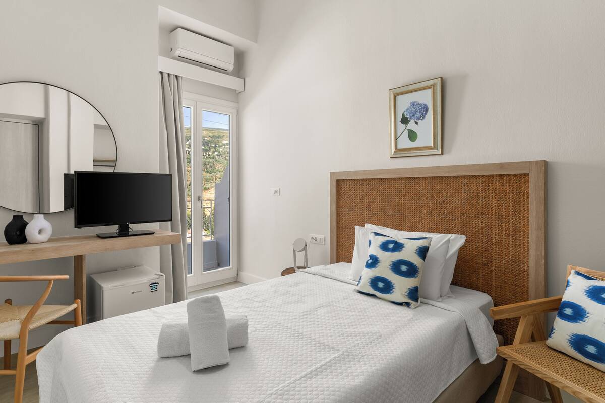 A hotel room with a bed, a desk with a computer, a chair, a TV, and a window with curtains.