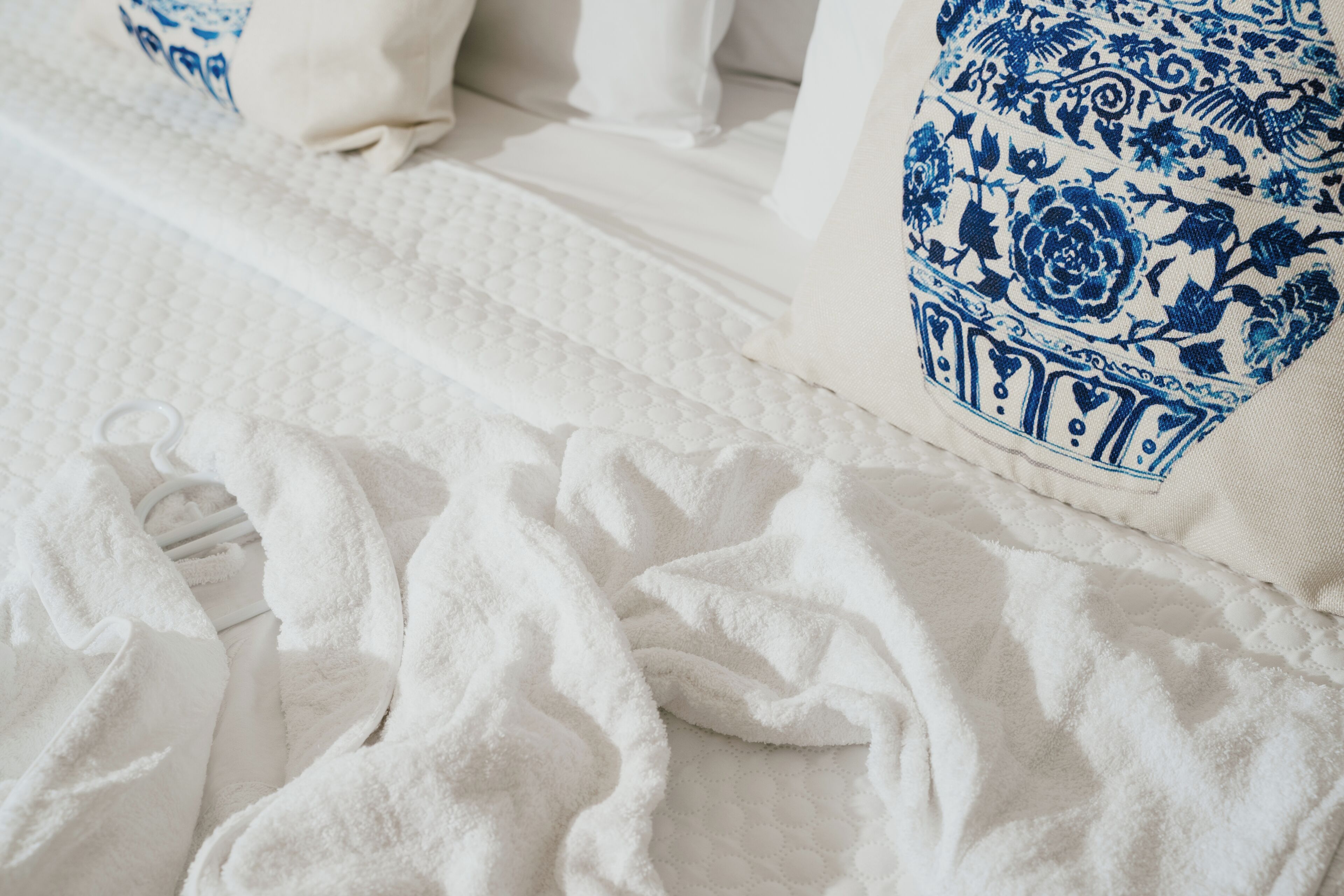 Een bed met witte lakens en blauwe kussens met bloemen.