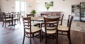 Un espace repas avec des tables et des chaises rondes, une cuisine à l’arrière-plan et un réfrigérateur à vin.