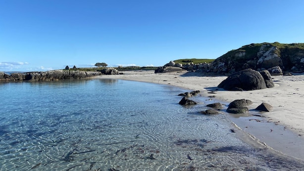 A beach with clear shallow waters, large rocks, and a grassy hill in the background. - Carna Bay Hotel (Carna)