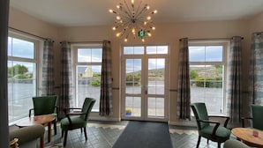 A hotel lobby with a modern chandelier, large windows with curtains, and green upholstered chairs. - Carna Bay Hotel (Carna)