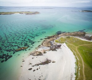Vue aérienne d’une zone côtière avec des eaux turquoise limpides, une plage de sable et un petit promontoire rocheux.
