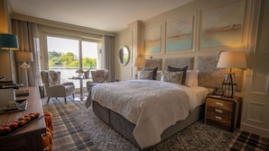 Een hotelkamer met een groot bed, een bureau met lamp, een stoel en uitzicht op de omgeving.