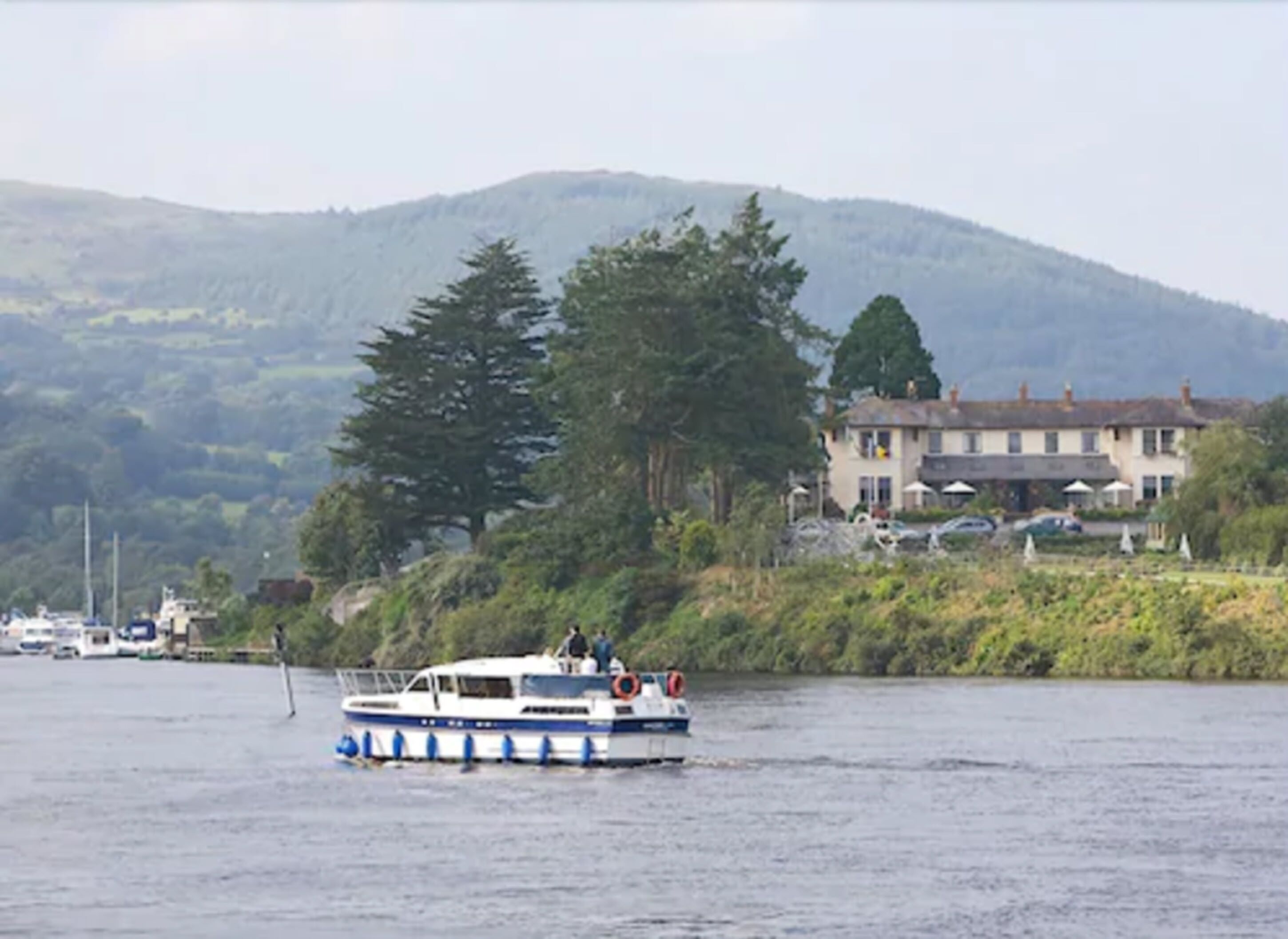 A boat on a river with a building and trees in the background.