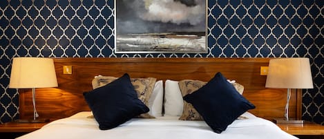 Ein Hotelzimmer mit einem hölzernen Kopfteil, zwei Nachttischlampen, einem großen Bett mit weißer Bettwäsche und einer Wand mit Muster.