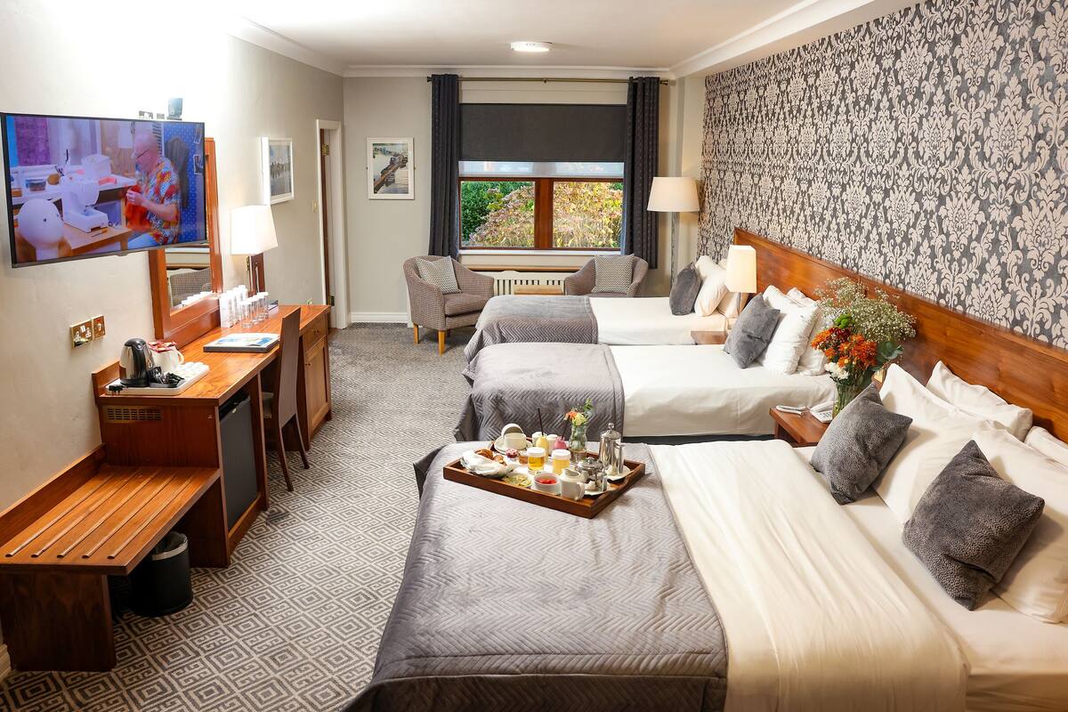 Une chambre d’hôtel avec deux lits, un bureau avec une machine à café, une télévision et une fenêtre avec des rideaux.
