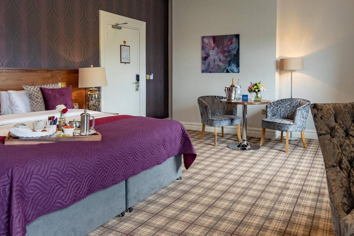 Une chambre d’hôtel avec un grand lit, une petite table sur laquelle est posé un vase de fleurs, une chaise et un canapé.