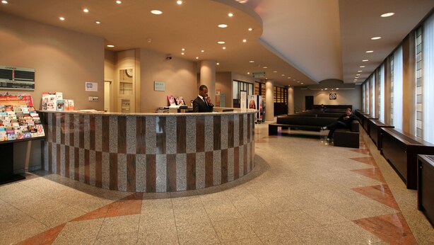 Een hotel receptie met een gebogen balie, een man achter de balie en een zithoek met uitzicht.