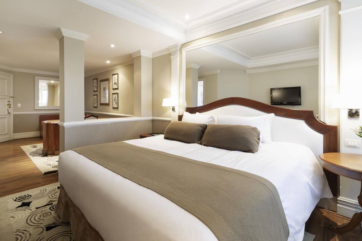 Una habitación de hotel con una cama grande, una mesita de noche, un espejo, un televisor y suelo de madera.