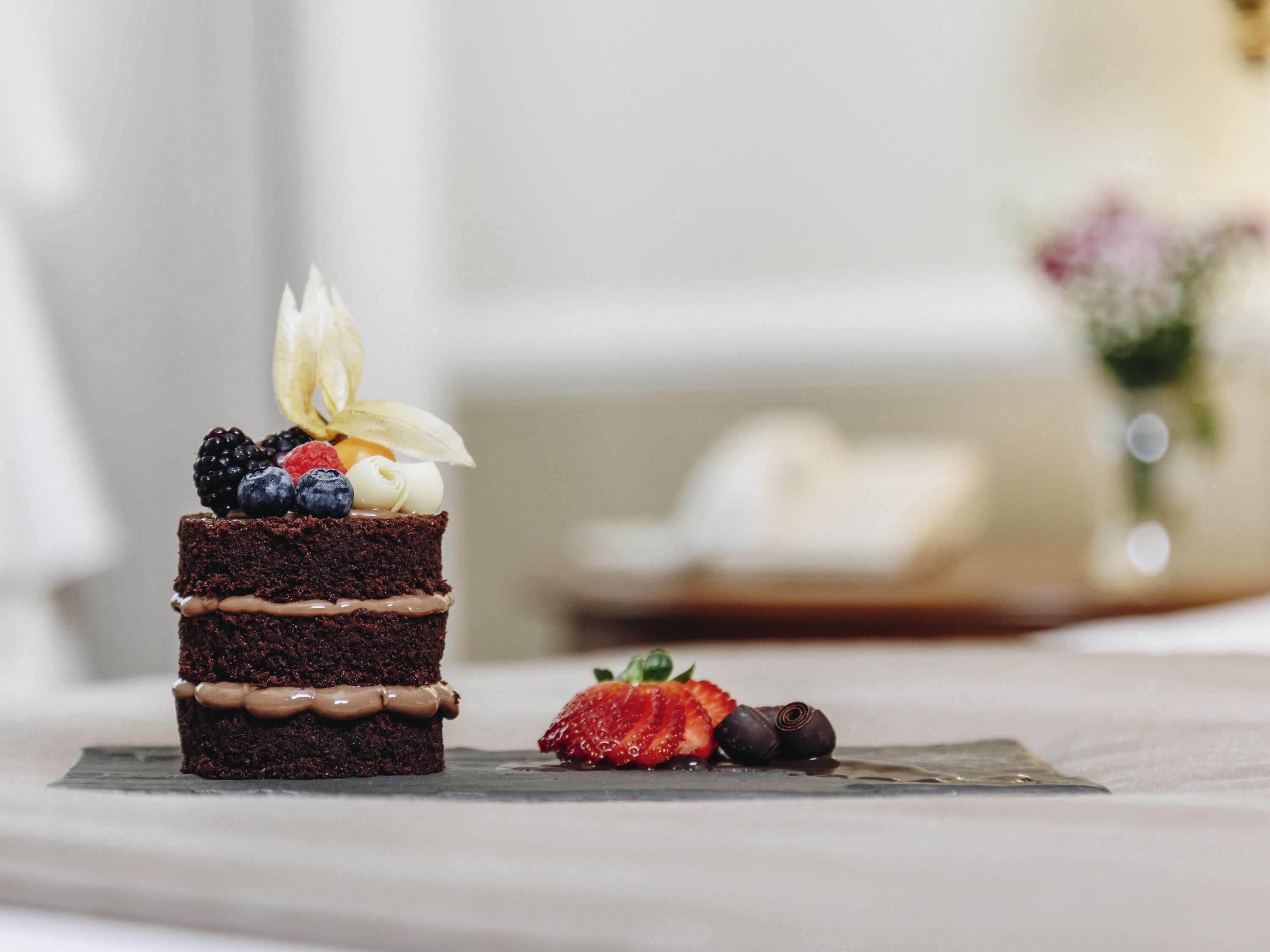 A chocolate cake with fruit and cream on a slate plate.