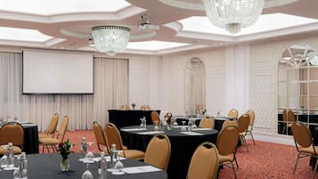 Un salón de conferencias con mesas redondas, sillas, una pantalla de proyector y candelabros.