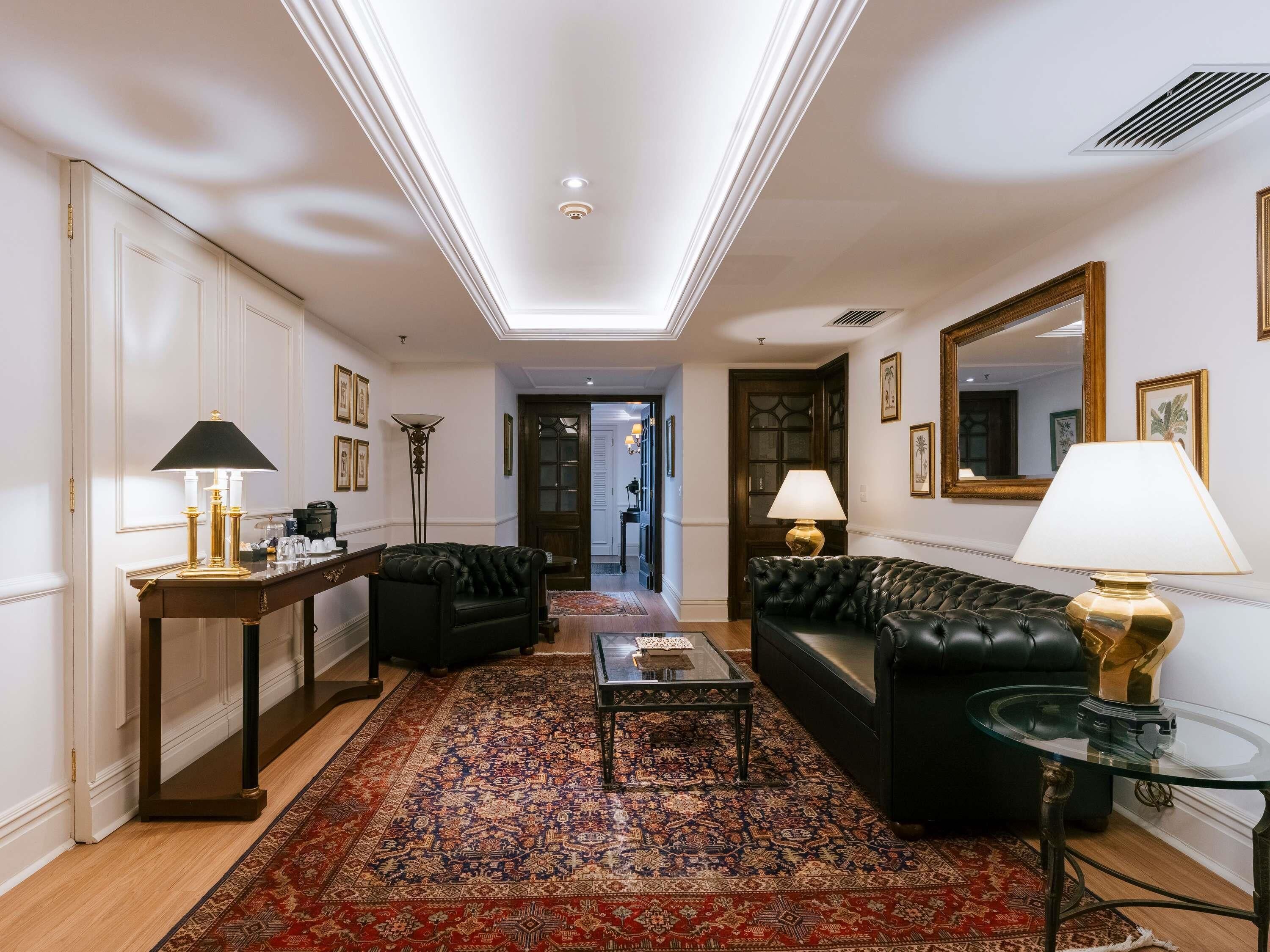 A spacious living room with a large rug, two black sofas, a glass coffee table, and a side table with a lamp.