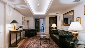 A spacious living room with a large rug, two black sofas, a glass coffee table, and a side table with a lamp.