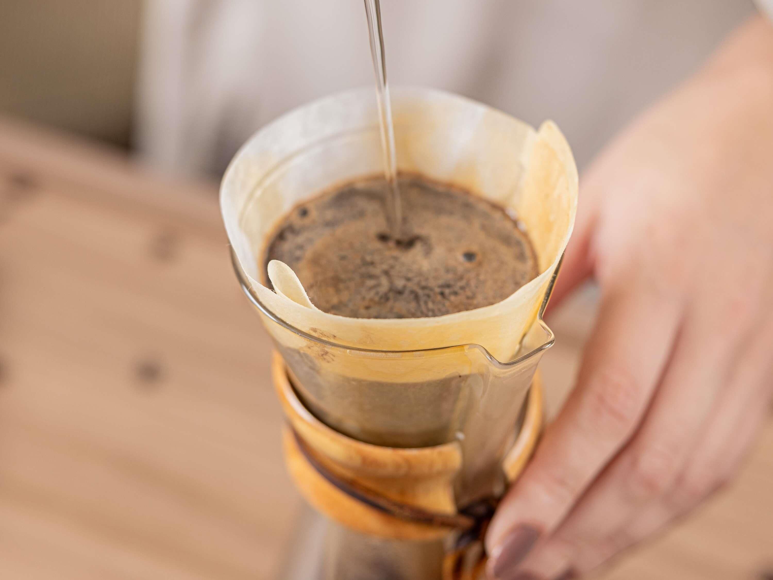 Una mano sosteniendo un gotero de café sobre una taza, con posos de café en su interior.
