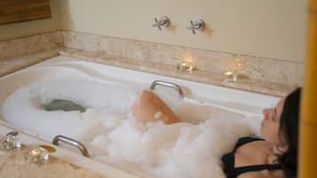Bathroom features a large bathtub, two faucets, and a lit candle.