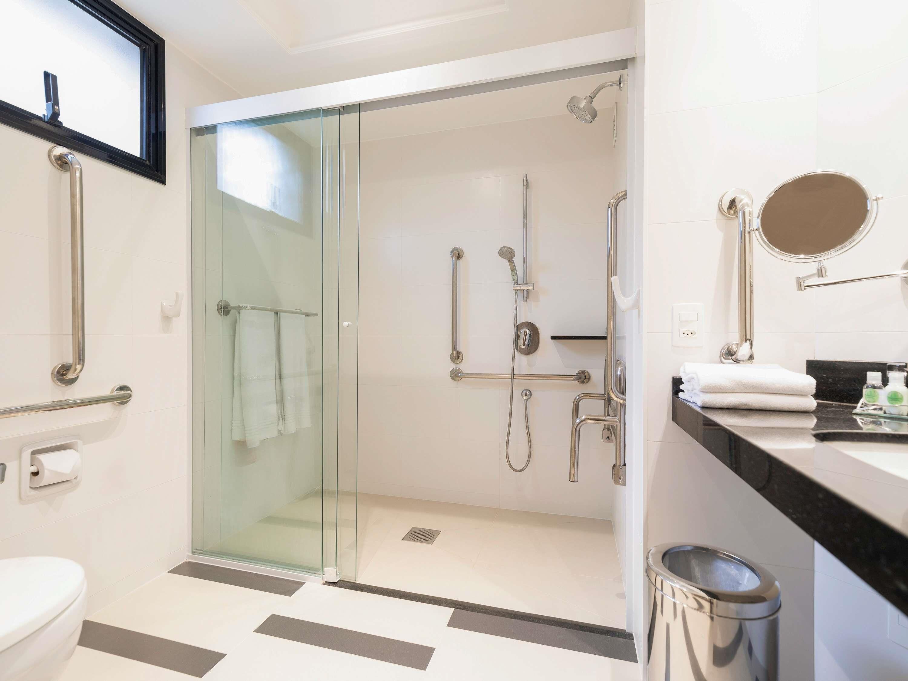 Un baño moderno con ducha envuelta en vidrio, inodoro, lavamanos con espejo y un cubo de basura.