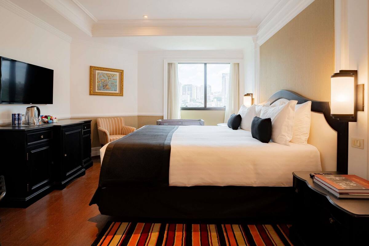 Habitación de hotel con cama, escritorio, televisión y ventana con vistas a la ciudad.