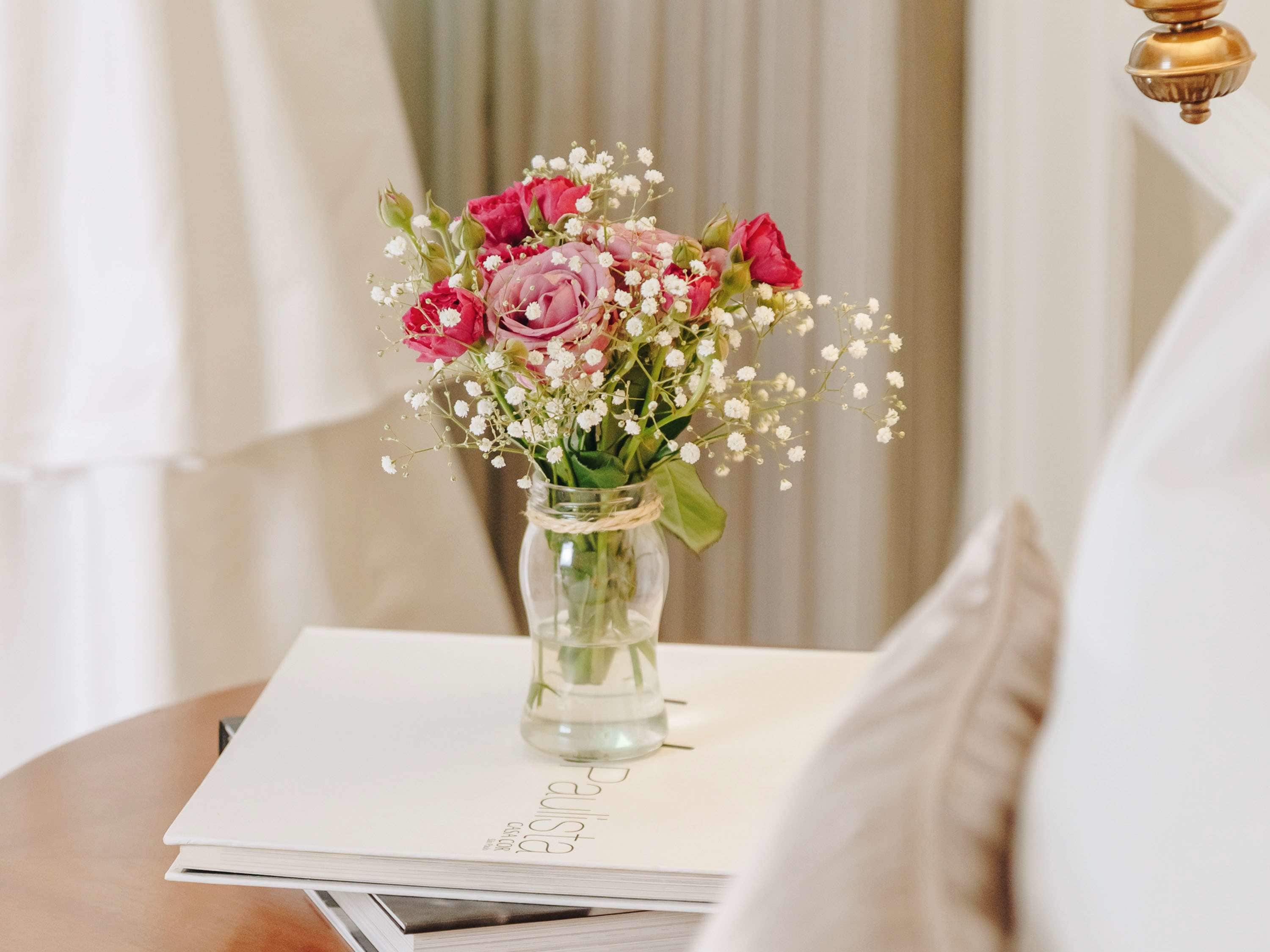 Un vase en verre transparent contenant des fleurs roses et rouges ainsi que du gypsophile, posé sur un livre blanc.