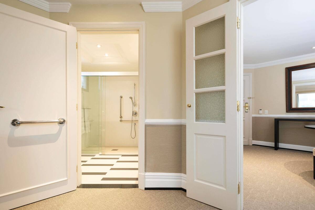 Habitación de hotel con cabina de ducha de vidrio, suelo a cuadros y puerta con paneles de vidrio esmerilado.