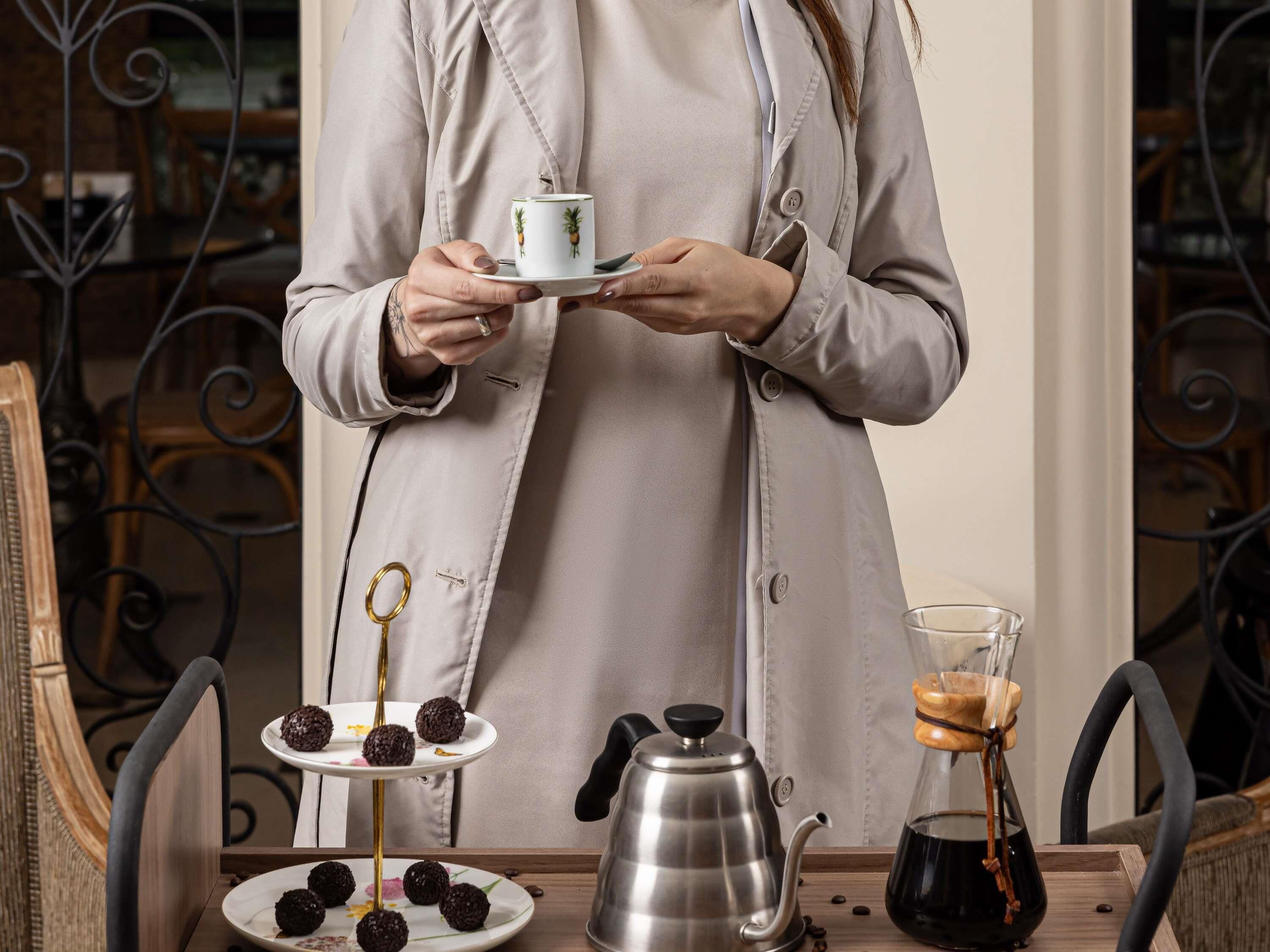 A person holding a teacup, a tray with food, a teapot, and a coffee pot.