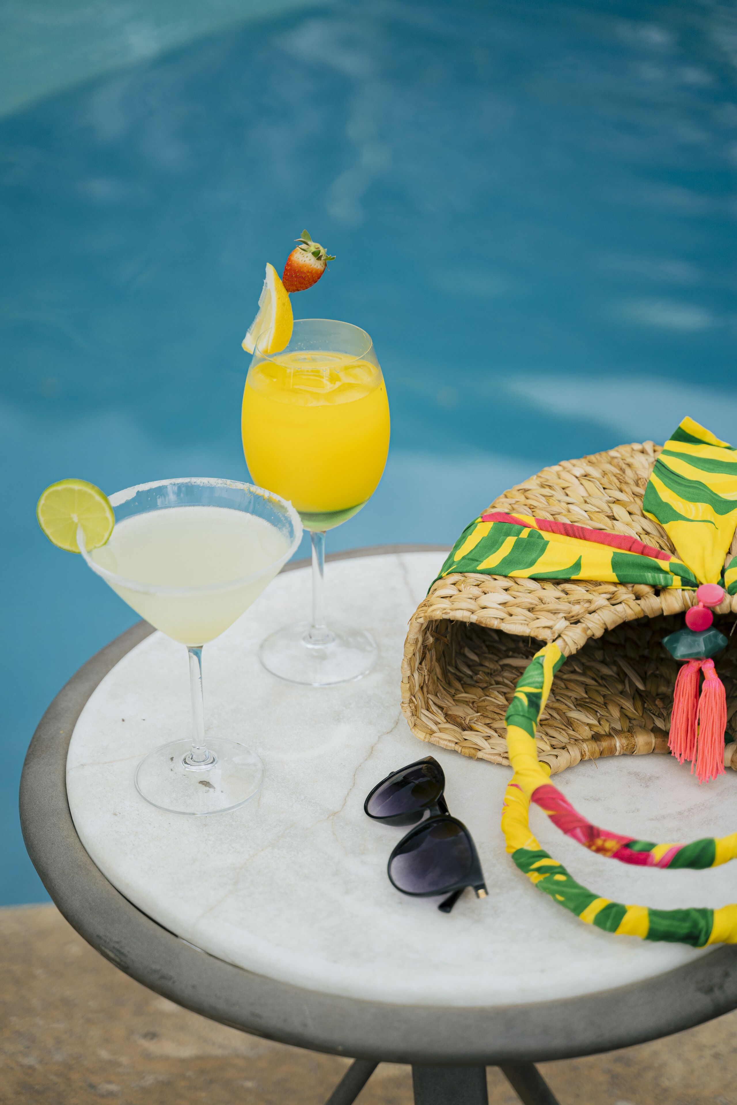 A table with two drinks, a straw hat, and sunglasses.