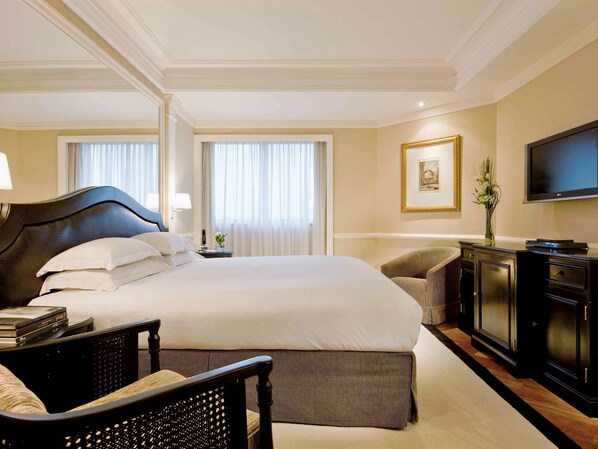 A hotel room with a large bed, a desk, a chair, a television, and a framed picture on the wall.