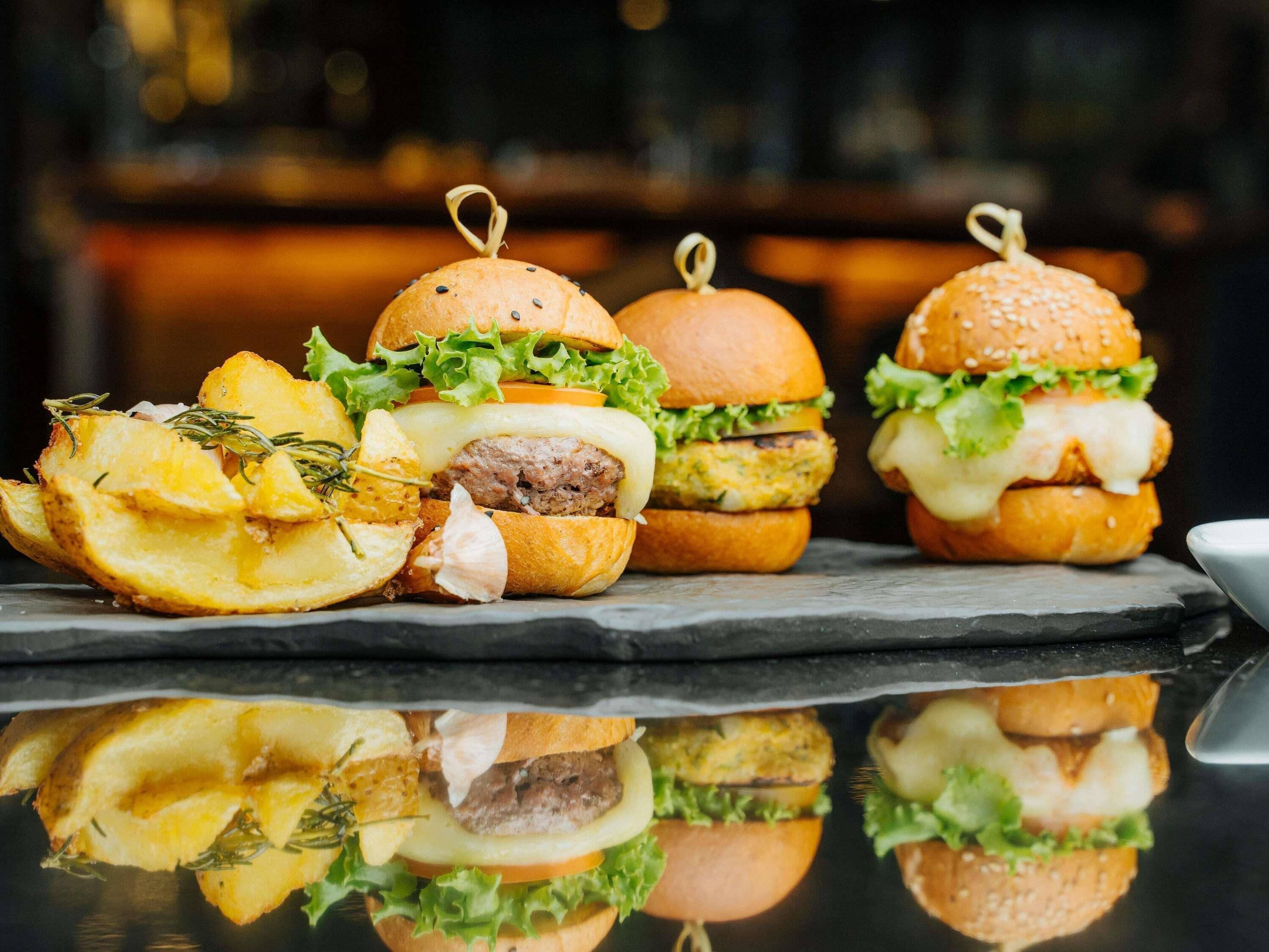 Three burgers with fries and a side of chips.