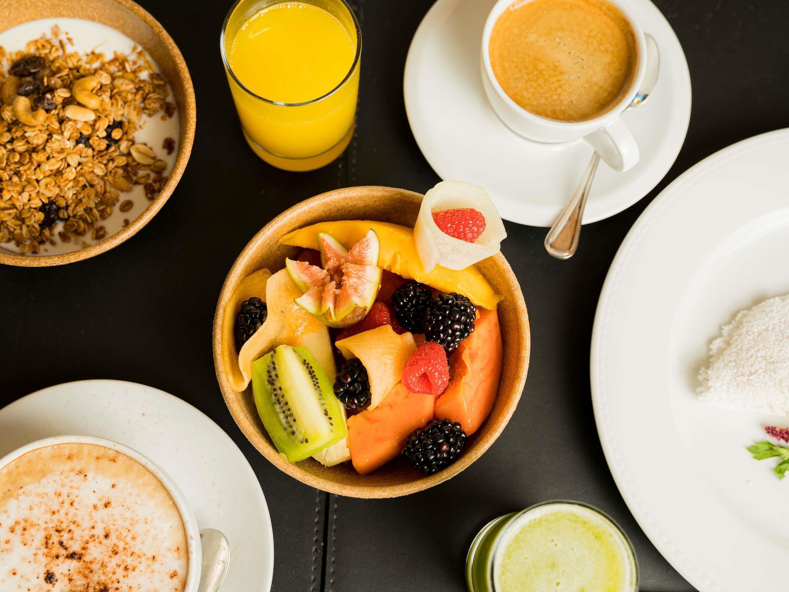Frühstückstisch mit einer Fruchtschale, einem Orangensaftglas, einer Kaffeetasse und einem Teller mit Granola.