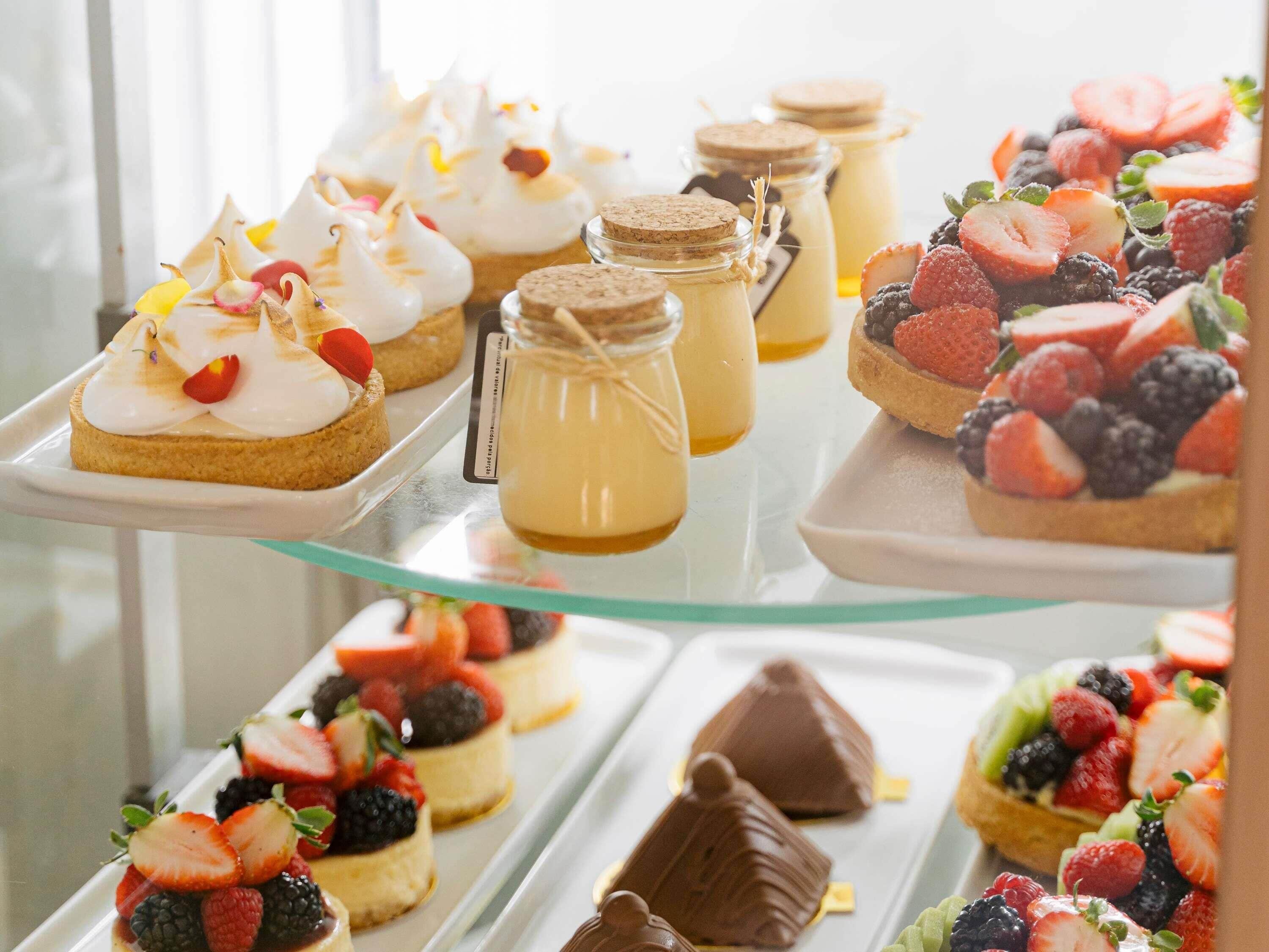 A variety of desserts on a glass display case, including meringues, fruit tarts, and chocolate treats.