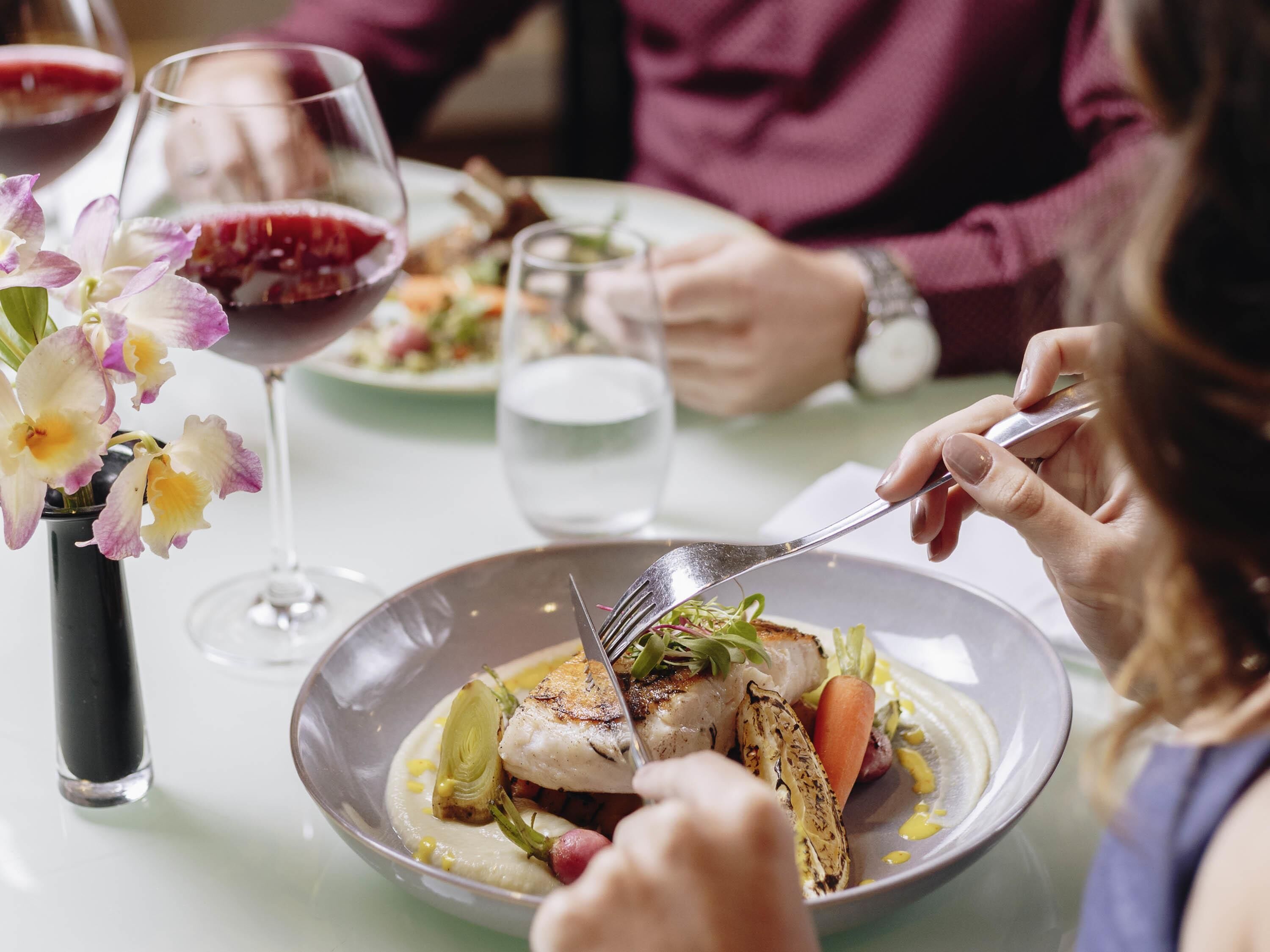Un tavolo da pranzo con un piatto di cibo, un bicchiere di vino rosso e un vaso di fiori.