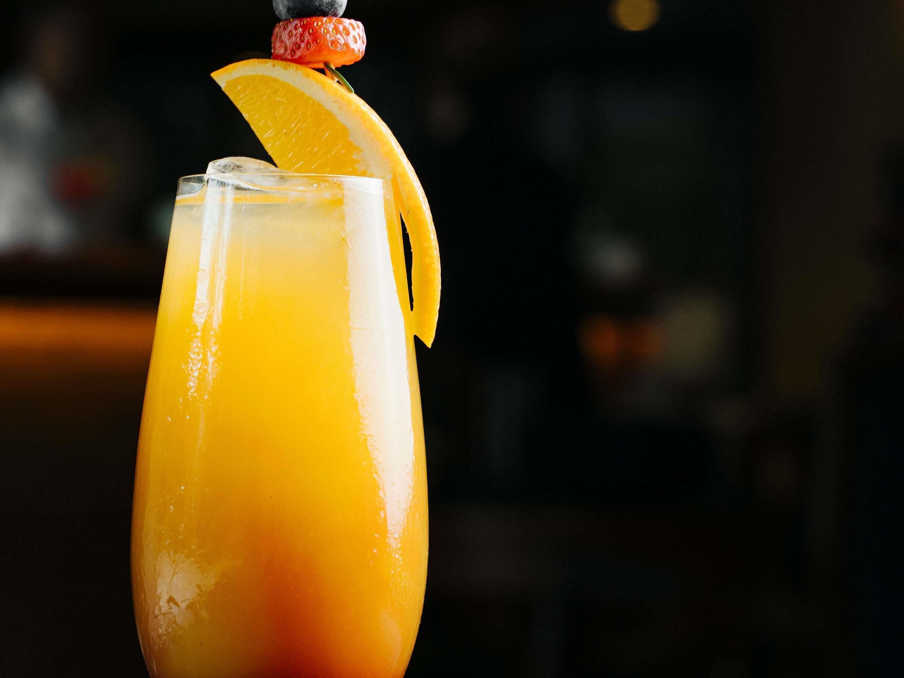 Un grand verre contenant une boisson jaune, décoré d’une fraise et d’une tranche d’orange.