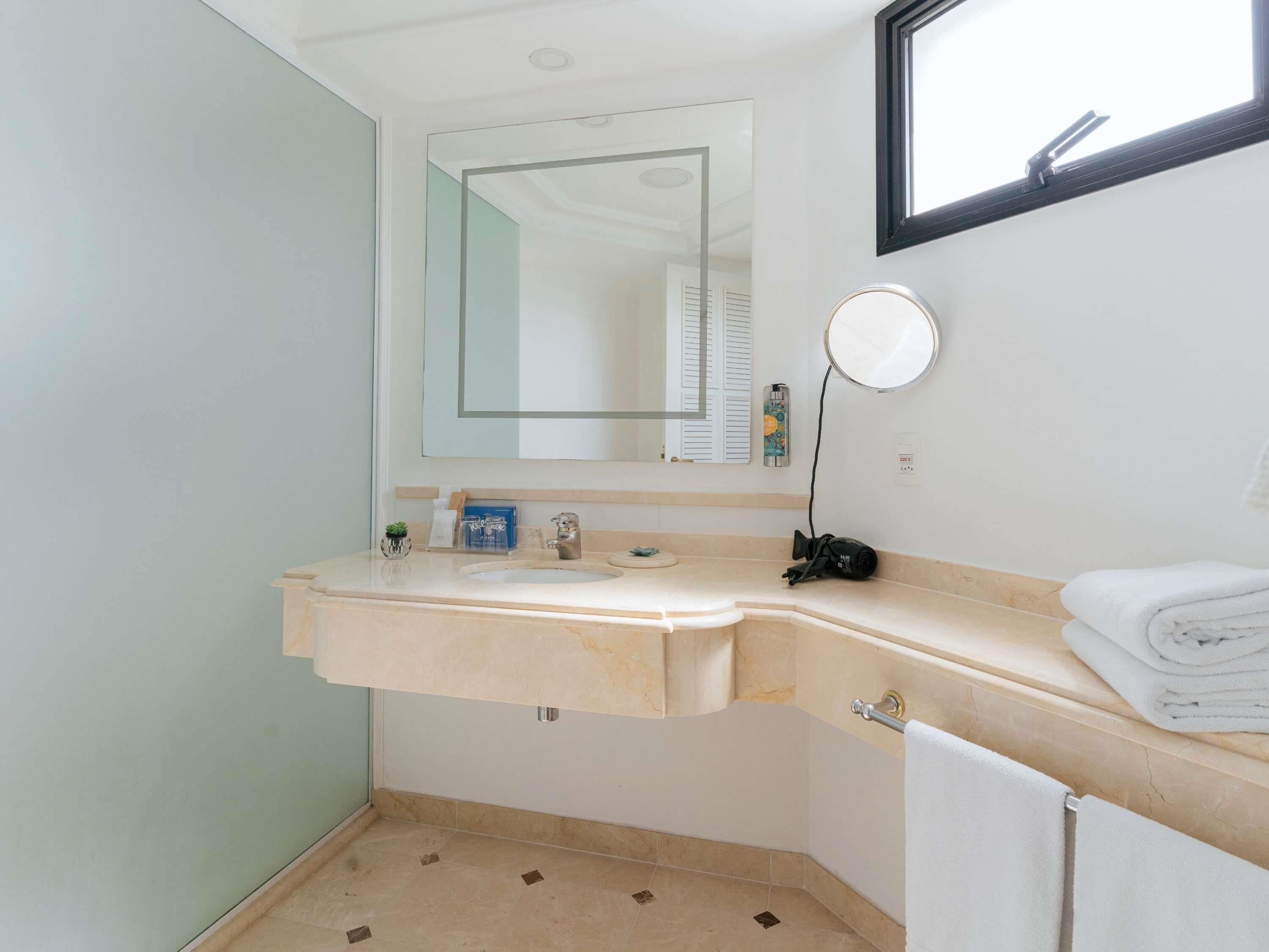 Een badkamer met een dubbele wastafel, een spiegel, een handdoekrek en een raam.