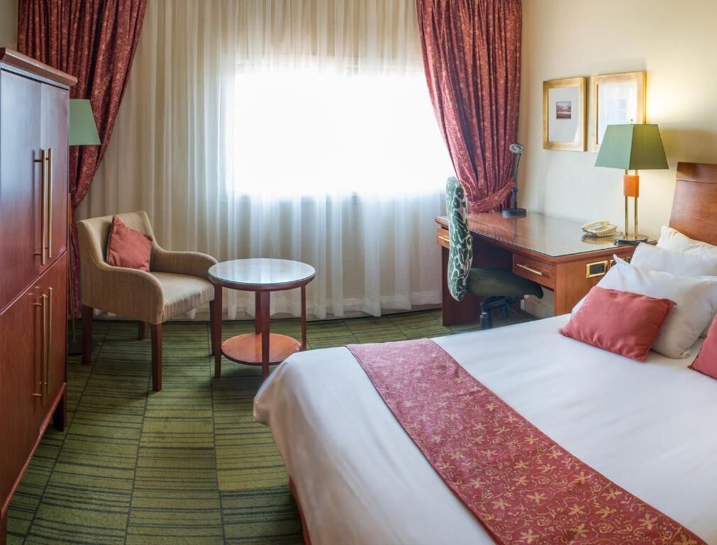A hotel room with a bed, a desk, a chair, a small table, and a wardrobe.