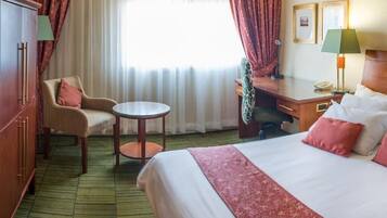 A hotel room with a bed, a desk, a chair, a small table, and a wardrobe.