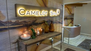 Vastaanottoalue, jossa on kyltti, jossa lukee »Camelot Spa», puinen vastaanottotiski ja taustalla kiviseinä.