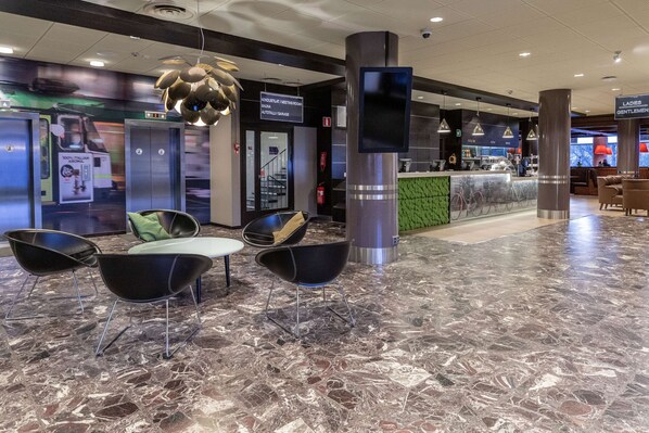 A modern lobby with a marble floor, black chairs, a reception desk, and a sign indicating a meeting room and garage.