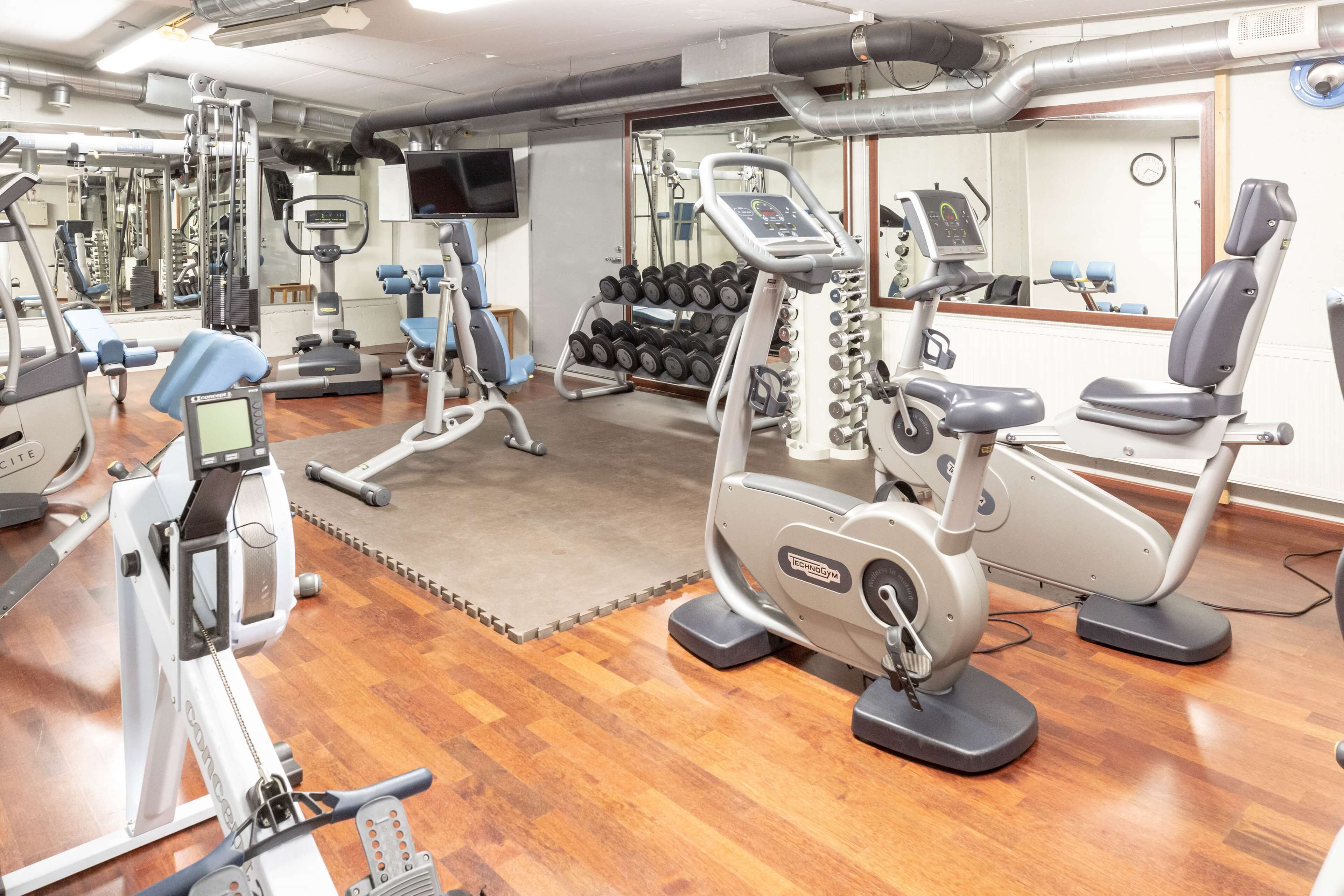 Een sportschool met cardioapparatuur, gewichthefmaterialen en een spiegel.