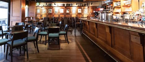 A bar area with wooden furniture, a counter with various items, and framed pictures on the walls.