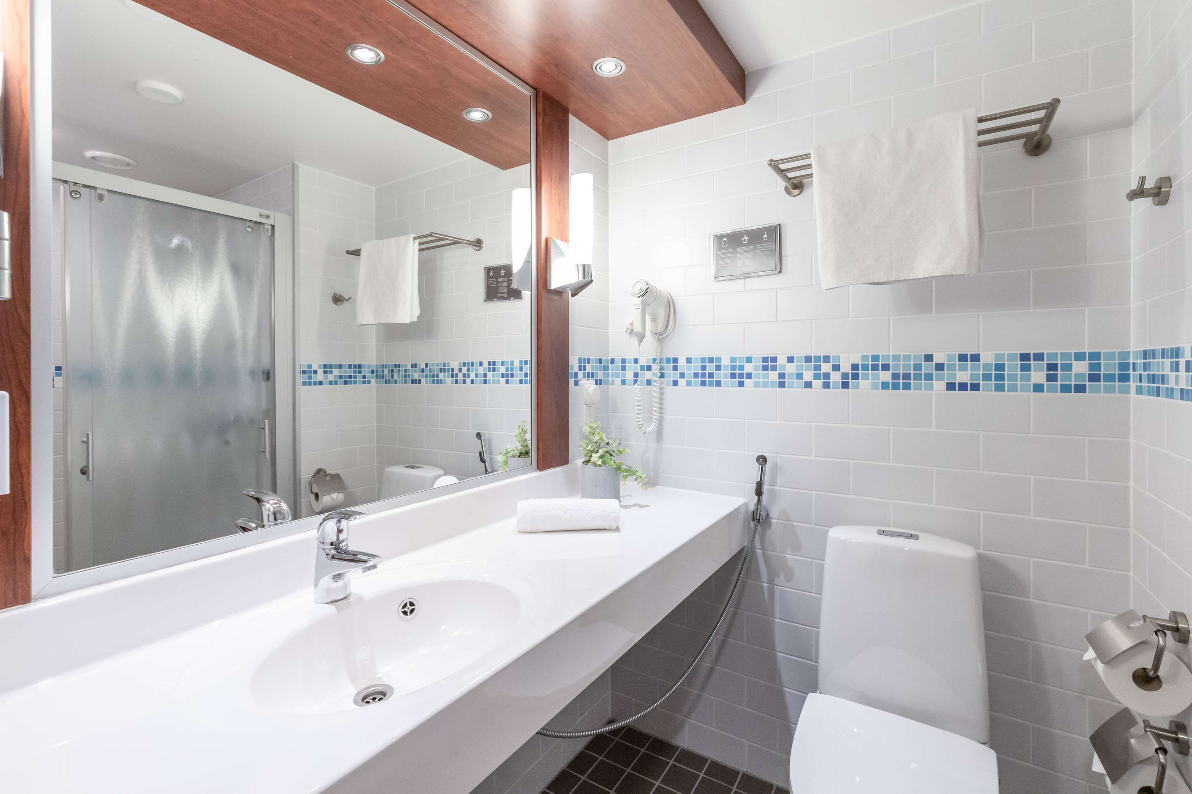 A modern bathroom with a large mirror, two sinks, a shower, and a toilet.