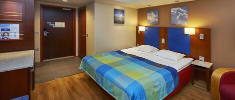 Habitación de hotel con cama, suelo de madera, puerta, una mesita y una silla.