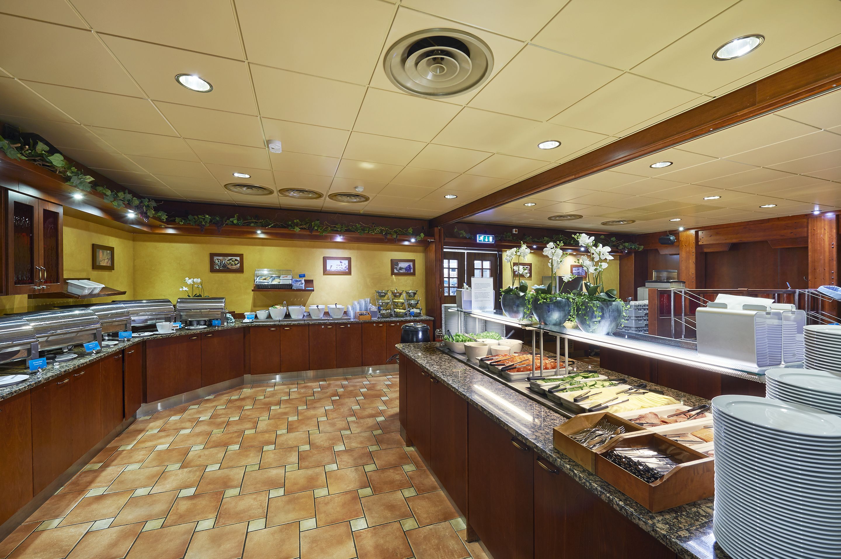 Uma área de buffet com vários pontos de serviço de comida, piso de azulejos e armários de madeira.