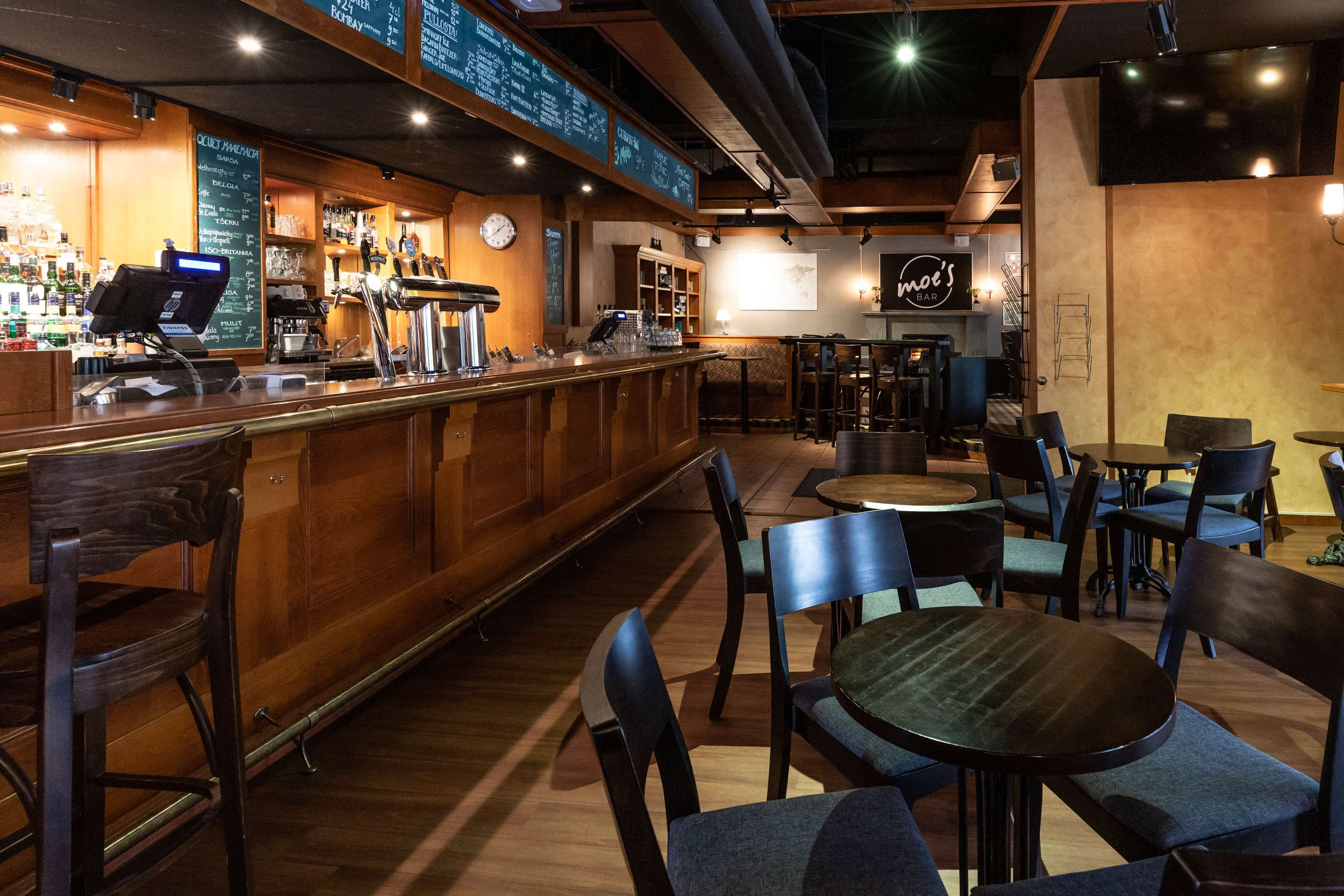 A bar area with wooden bar counters, seating arrangements, and a menu board.