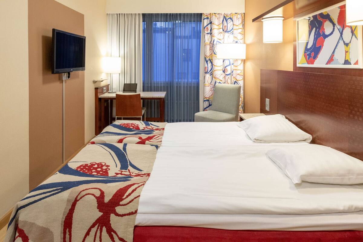 Una habitación de hotel con cama, escritorio, silla y televisor en la pared.