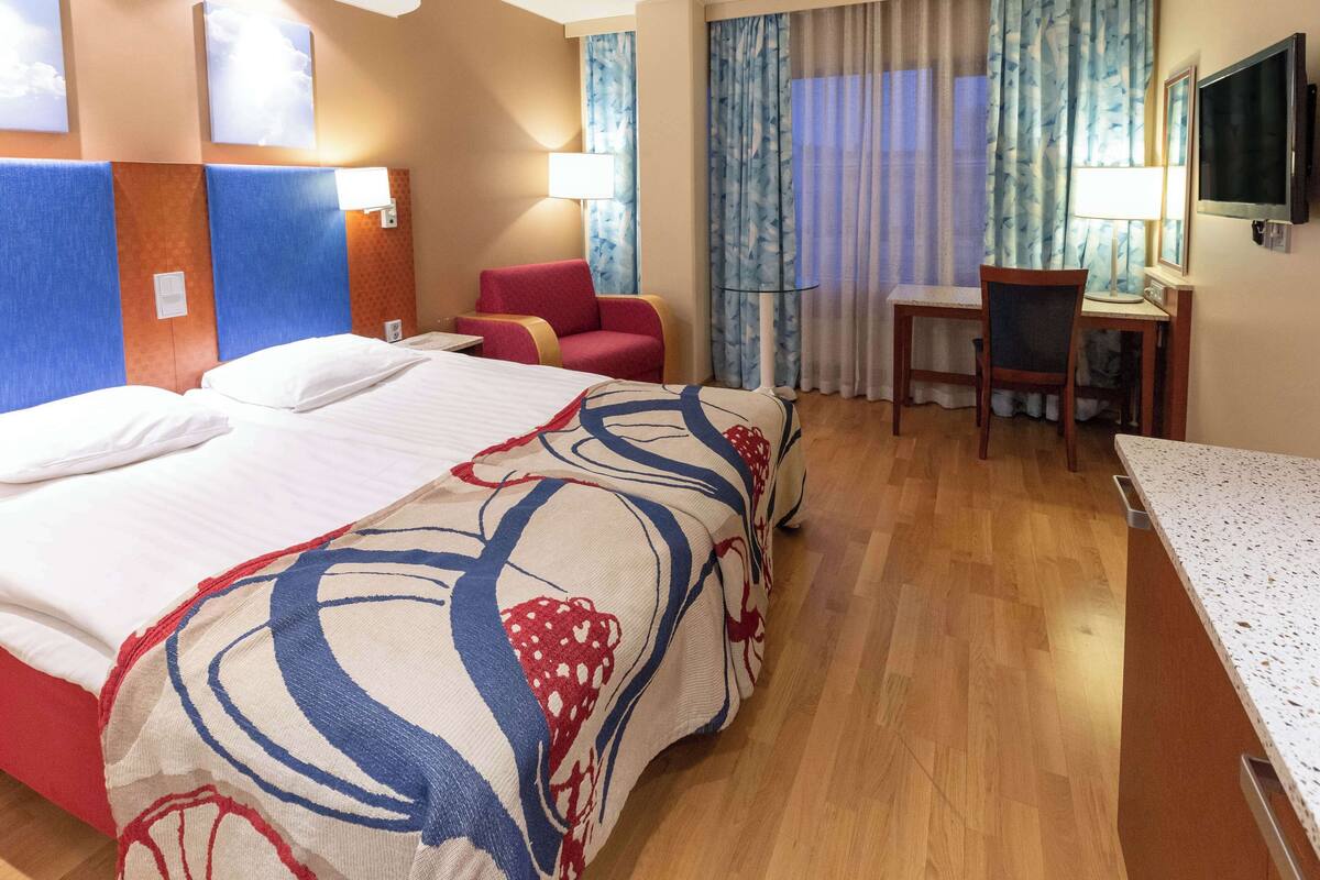 Una habitación de hotel con una cama grande, un escritorio, una silla y un televisor.