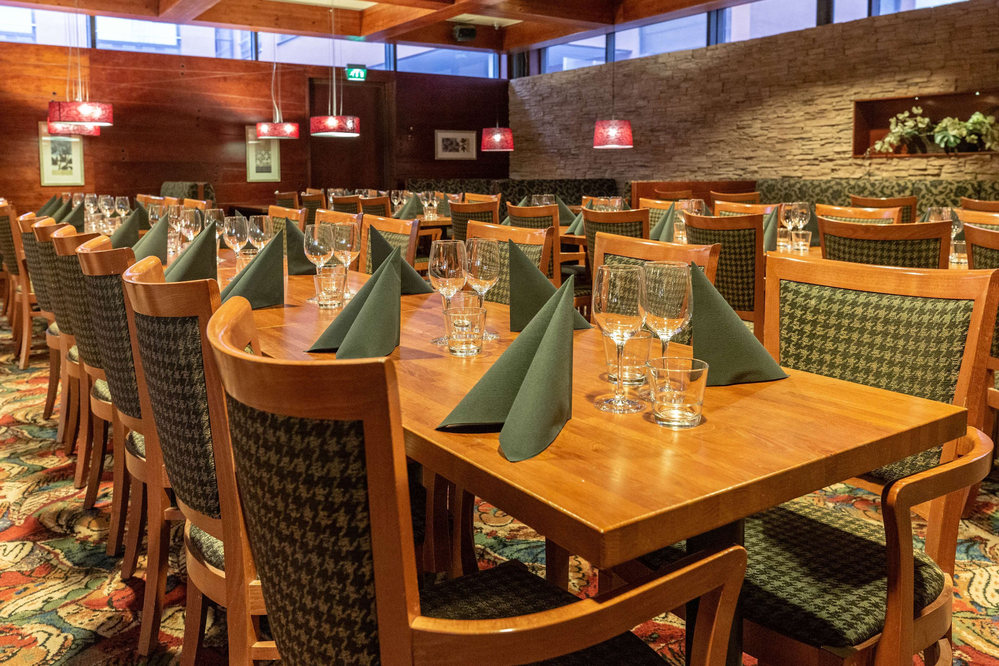 En restaurant med træborde og -stole, grønne servietter og røde hængelamper.