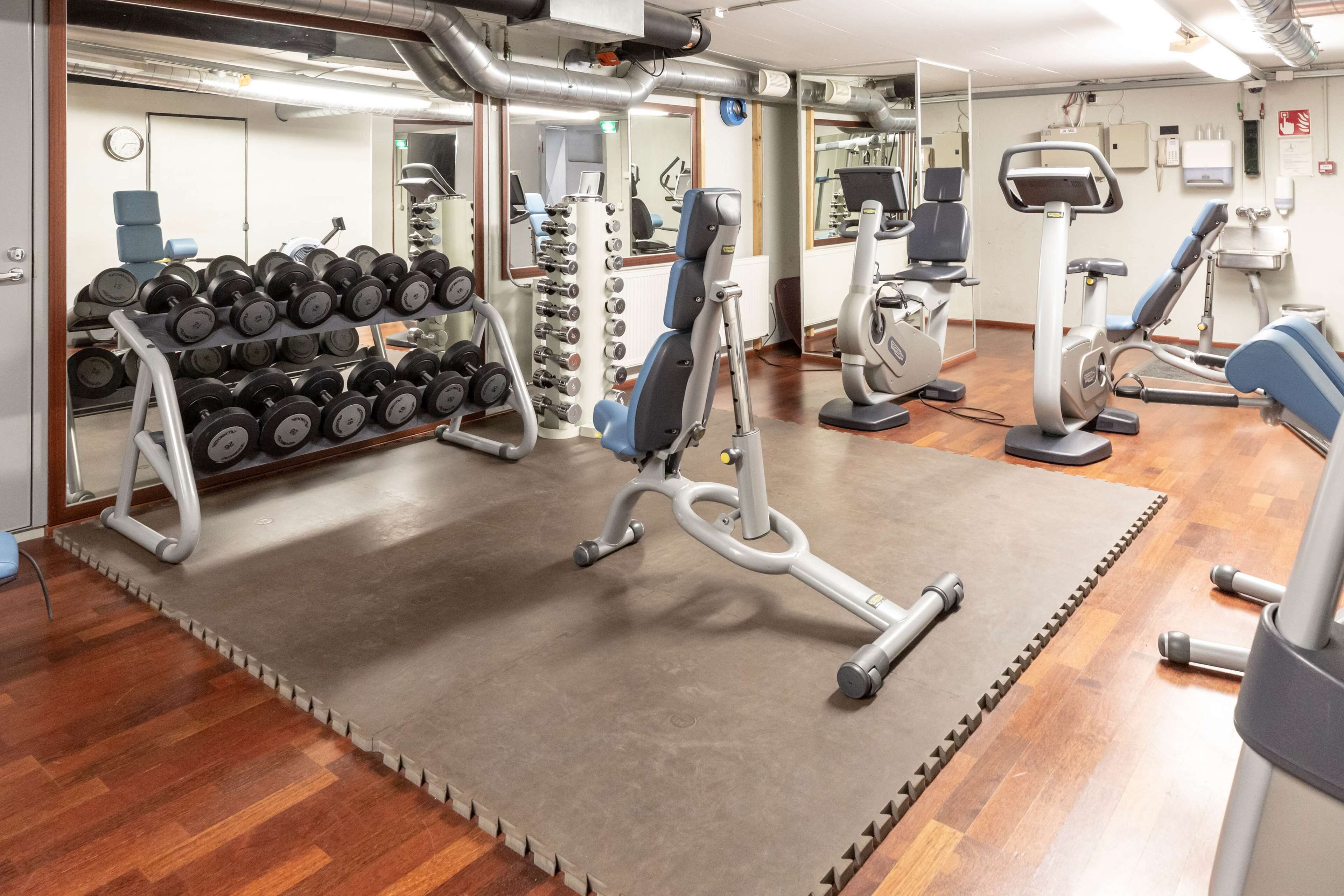 A gym with exercise equipment, a rack of dumbbells, and a mirror.