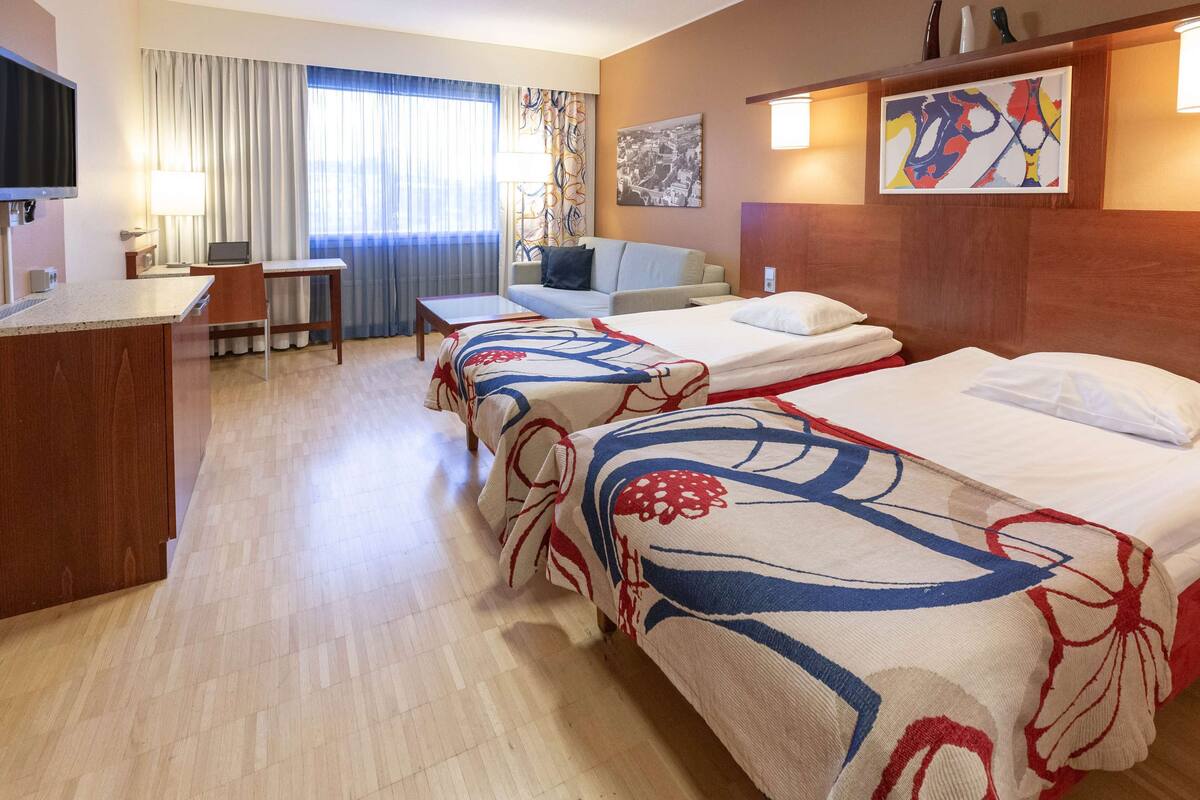 Habitación de hotel con dos camas, un escritorio, una silla, un televisor y una ventana con cortinas.