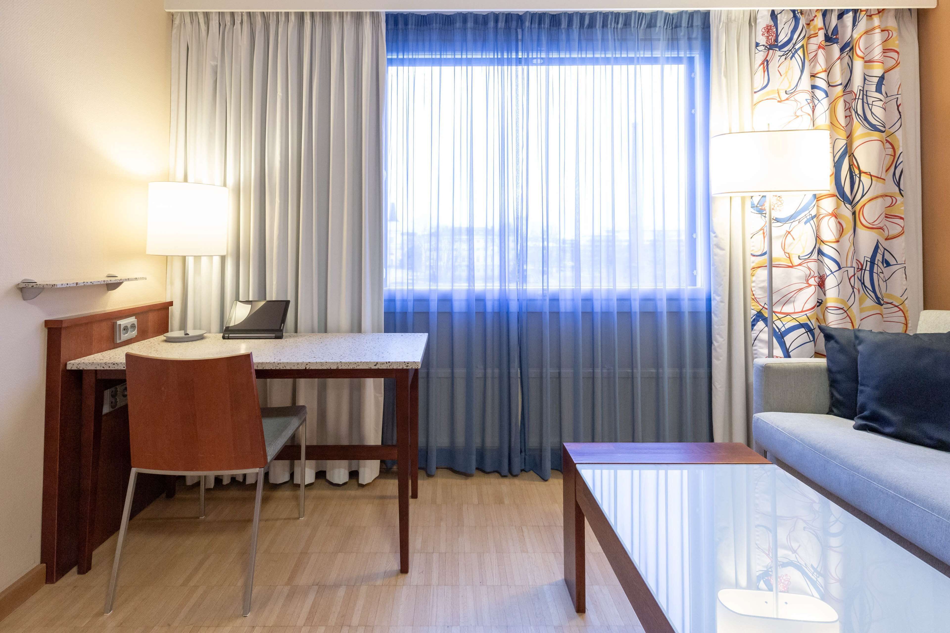 A hotel room with a desk, chair, and a sofa.