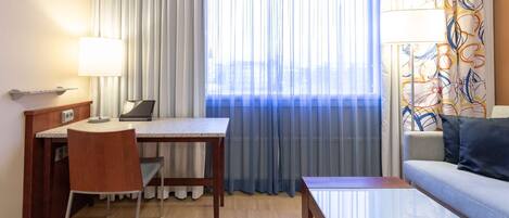 A hotel room with a desk, chair, and a sofa.