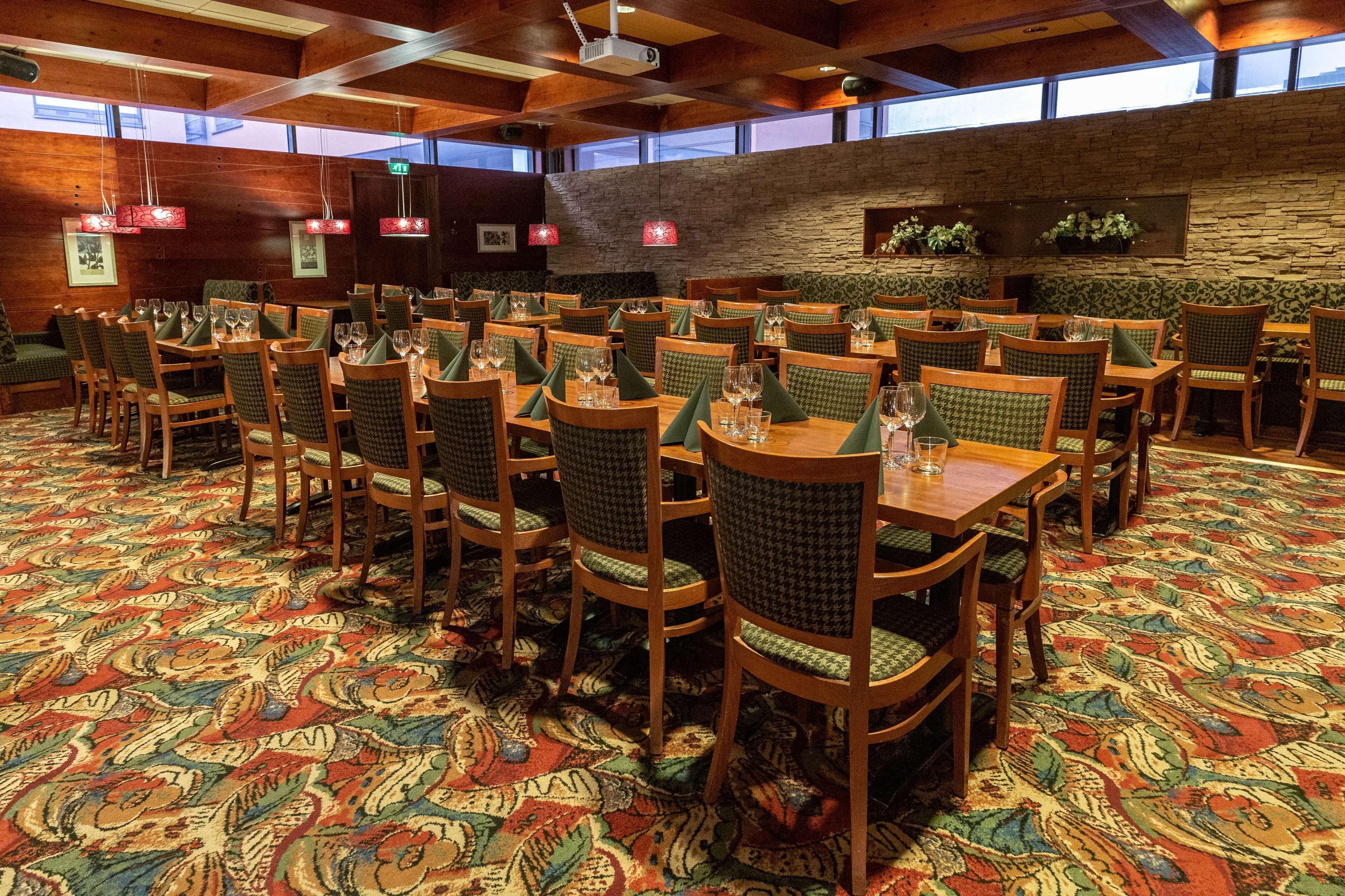Un vaste espace dédié à la salle à manger, avec de nombreuses tables et chaises, une moquette à motifs, des murs en bois et des luminaires suspendus.